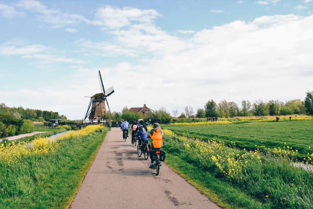Famiglia durante un viaggio in bici Girolibero su ciclabile in Olanda con vista di un mulino a vento sullo sfondo